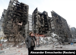 Egy nő áll egy lerombolt utcán Mariupolban 2022 márciusában