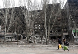 Câțiva localnici din Mariupol trec pe lângă un bloc distrus de bombardamentele rusești, 31 martie 2022.