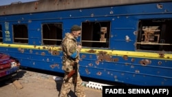 Ukrán katona egy szétlőtt vonat mellett Trosztyanecben 2022. március 29-én