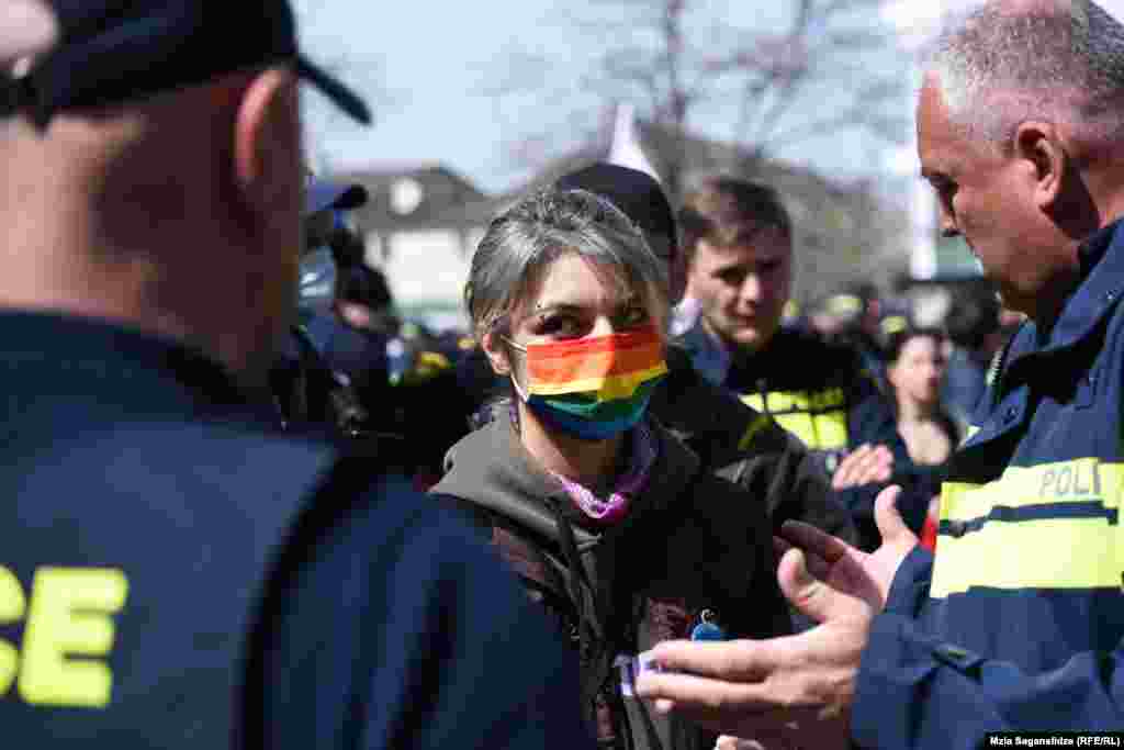Саломе Баркер, облечена во ЛГБТ маска пред Градскиот суд во Тбилиси на 4 април, ја гледа полицијата додека ја чека пресудата на уапсените под обвинение за насилство врз новинари. Апсењата следеа по собирот на 5 јули 2021 година, против планираниот марш на гордоста на ЛГБТ во грузискиот главен град, кој стана насилен бидејќи демонстрантите нападнаа активисти и новинари, вклучително и двајца новинари на РСЕ. (Мзија Саганелиџе РСЕ)