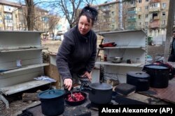 Egy nő főz az udvaron az aknatűzben megrongálódott lakóházak között, Mariupol peremén, amelyet a szeparatista Donyecki Népköztársaság harcosai ellenőriznek. Ukrán illetékesek szerint a kollaboránsok miatt sikerült gyorsan kiiktatni a város infrastruktúráját