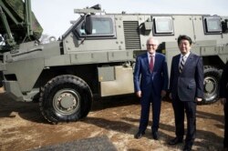 Ausztrália és Japán korábbi miniszterelnökei egy Bushmaster páncélozott jármű elött 2018-ban