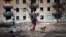 A man walks with his dog near an apartment building damaged by shelling on the outskirts of Mariupol. 