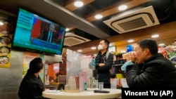 Люди дивляться телевізор, де транслюють новини про напад російських військ на Україну в ресторані в Гонконзі 24 лютого 2022 року