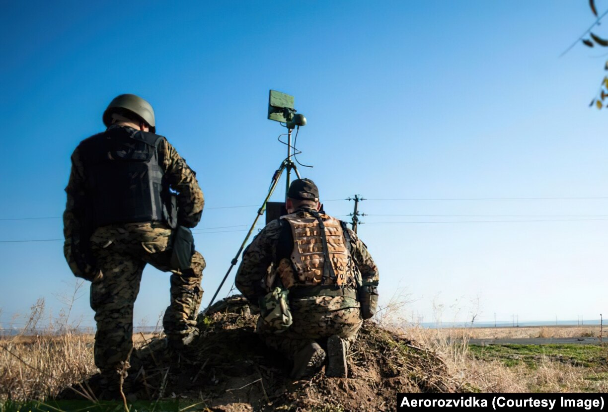 Ukrainian servicemen train with drones before the 2022 Russian invasion. The men are viewing a screen showing real-time video feed from an octocopter, while a tripod-mounted transmitter communicates with the drone.