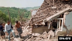 People pass by one of the destroyed houses in the village of Ripanj, near Belgrade, that was destroyed during NATO air raids in May 1999.