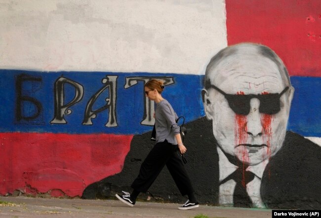 Një grua duke kaluar pranë një murali të presidentit rus, Vladimir Putin. Në muralin që pastaj është lyer me ngjyrë, shkruan "Vëllai". Beograd, 7 maj 2022.