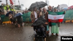 گروهی از حوثی‌ها در حالی که پرچم ایران را در دست گرفته‌اند، زیر باران در تظاهرات ضد عربستان سعودی در صنعا، پایتخت یمن، شرکت کرده‌اند