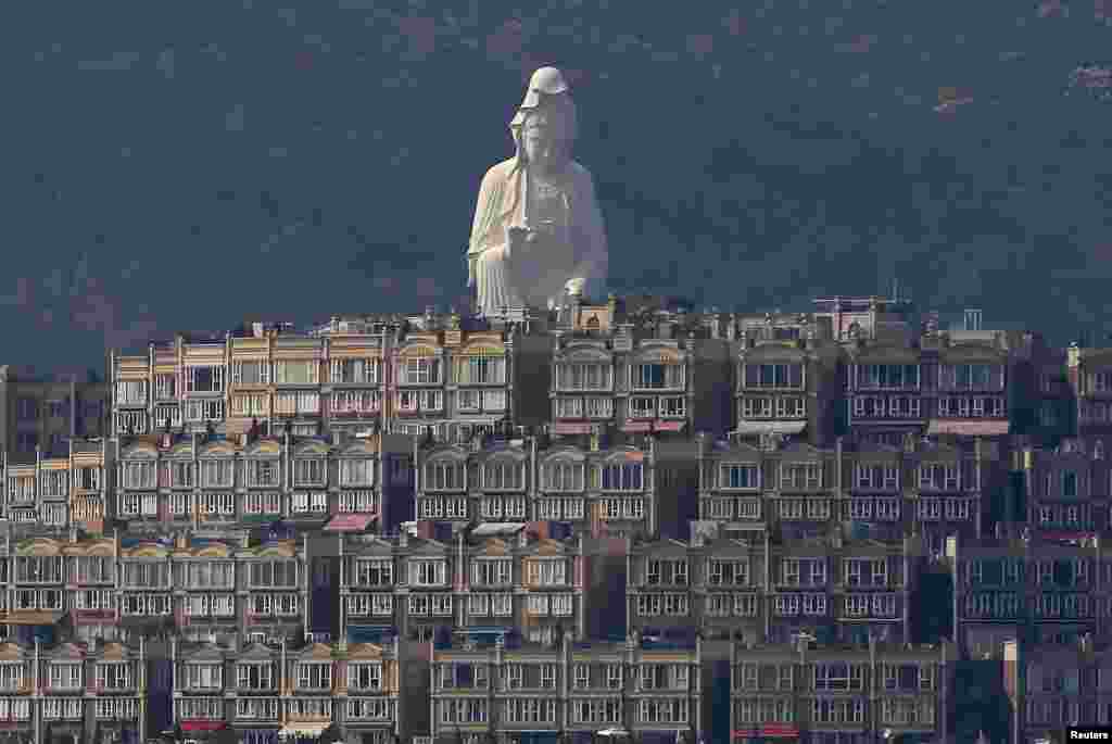 A 76-meter-high bronze-forged white Buddhist Avalokitesvara or Guan Yin statue, part of the Tsz Shan Monastery, stands behind luxury homes in Hong Kong. (Reuters/Bobby Yip)