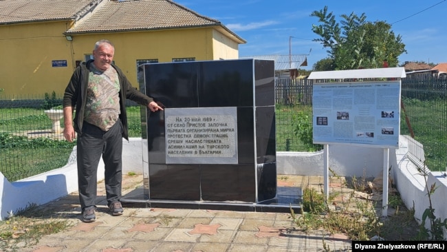 Зикри Солак показва плочата в село Пристое в памет на мирния протест на българските мюсюлмани, протестирали през май 1989 срещу насилствената им асимилация, предприета от комунистическия режим. Протестите в Пристое и на други места стават известни под името "майски събития".