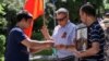 Молодой человек вручает казахстанские ленты небесно-голубого цвета мужчине с георгиевской лентой (организаторы шествия в День Победы призывали участников не использовать эту символику) на груди и красным знаменем в руках. Алматы, 9 мая 2022 года