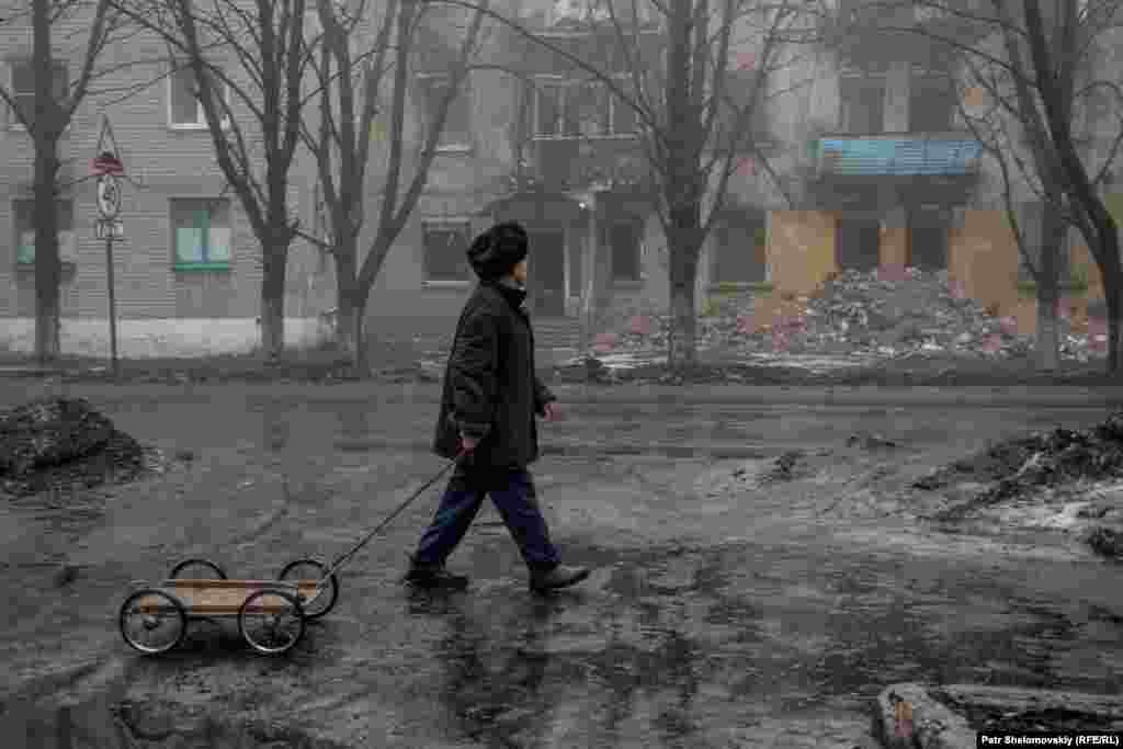Мужчина с тележкой идет рядом с разрушенным зданием в Дебальцеве.