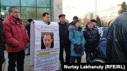 Азаматтық белсенді Дулат Ағаділ Нұр-Сұлтандағы тергеу абақтысында жұмбақ жағдайда қаза болғаннан кейін Алматы полиция департаменті алдына наразылық білдіріп жиналған адамдардың бірі "Мұхтар Жәкішев босатылсын!" деген плакат ұстап тұр. 25 ақпан 2020 жыл.
