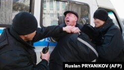 Полиция ходимлари митинг иштирокчиларидан бирини қўлга олиб, полиция бўлимига олиб кетиш учун машинага ўтиришга мажбурламоқда. Олмаота, 2020, 1 март. 