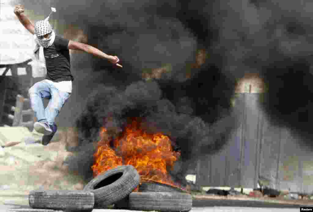 A Palestinian jumps over burning tyres during clashes with Israeli troops in the West Bank city of Hebron on July 31. (Reuters/Mussa Qawasma)