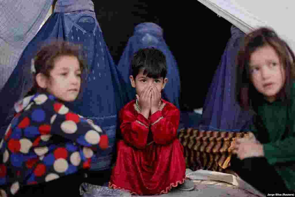 Afghan girls and burqa-clad women who are among the displaced families fleeing violence in their provinces sit in front of a tent at a makeshift shelter in the Shahr-e Naw park in Kabul on October 4.