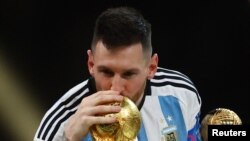 Lionel Messi sărută cel mai important trofeu al carierei sale, în timp ce ține în mână premiul Balonul de Aur, după ce a câștigat Cupa Mondială din Qatar, pe stadionul Lusail, 18 decembrie 2022.