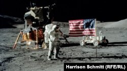 Юджийн Сърнън козирува пред американското знаме. Зад него е лунният модул, а вдясно се вижда и луноходът.