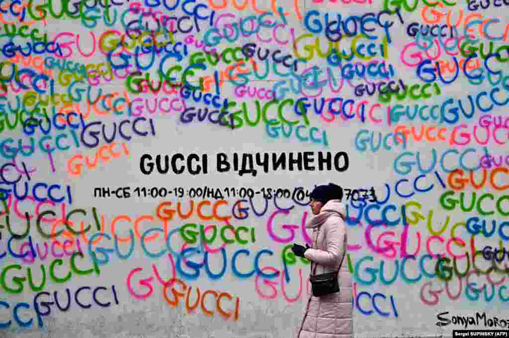 A woman walks past the Gucci fashion house shop window, which is covered with chipboard to protect against shelling fragments, with a sign reading, &quot;Gucci is open,&quot; in the center of Kyiv on December 12.