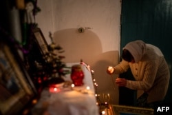 Vjernica pali svijeću tokom pravoslavne božićne mise u podrumskom skloništu u Časivu Jaru