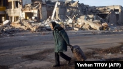 Egy idős nő kerekes bevásárlótáskát húz egy lerombolt épület mellett az ukrajnai Donyecki területen található Bahmutban 2022 decemberében