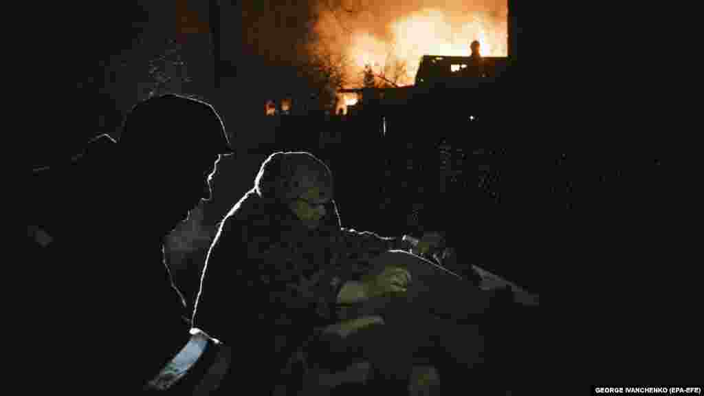 O ucraineancă strânge niște lucruri lângă o clădire în flăcări, după un bombardament rusesc în satul Ivanivka lângă Bahmut, Donețk, Ucraina
