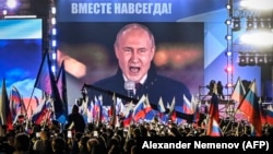 Președintele rus Vladimir Putin, văzut pe un ecran în Piața Roșie din Moscova, în septembrie 2022, în timp ce se adresează mulțimii despre așa-zisa reunire cu Rusia a patru regiuni parțial ocupate din Ucraina.