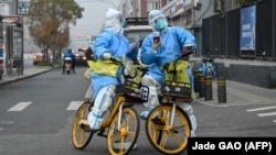 Punonjësit shëndetësorë me pajisje mbrojtëse kundër COVID-19 duke lëvizur me biçikleta përgjatë një rruge në Pekin. 24 nëntor 2022.