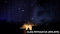 A man stands near burning garbage in front of an apartment building during a scheduled power cut in Kyiv.