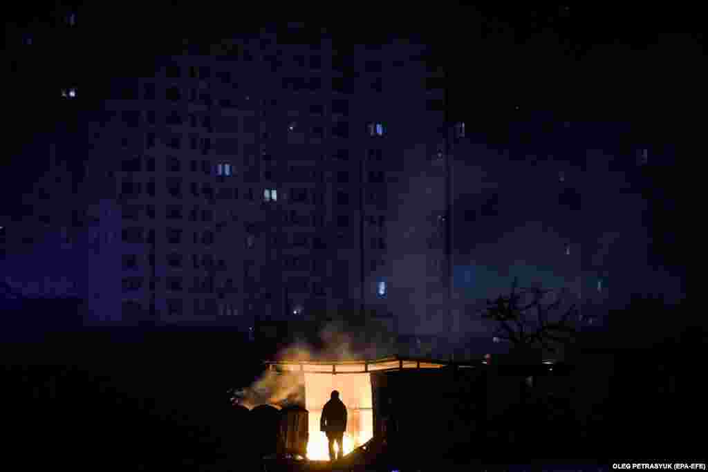 Мужчына стаіць каля падпаленага сьмецьця перад жылым домам падчас плянавага адключэньня электрычнасьці ў Кіеве.