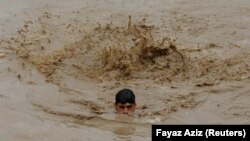 A man swims in floodwaters while heading for higher ground during the monsoon season in Charsadda, Pakistan, on August 27, 2022.