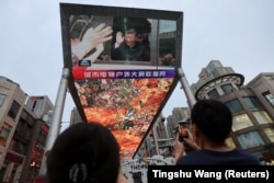 A giant screen broadcasts news footage of Chinese President Xi Jinping visiting the Xinjiang Uyghur Autonomous Region, at a shopping center in Beijing on July 15, 2022.