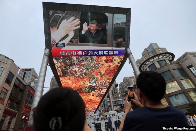 A giant screen broadcasts news footage of Chinese President Xi Jinping visiting the Xinjiang Uyghur Autonomous Region, at a shopping center in Beijing on July 15, 2022.