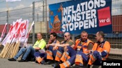 Radnici sede ispod transparenta na kojem piše "Zaustavite minstruma inflacije" u luci u Hamburgu, Nemačka, 9. juni 2022. 