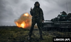 Український військовий позує для фото, коли його колеги ведуть вогонь із трофейного танка Т-80 по позиціях армії РФ на Донеччині, 22 листопада 2022 року