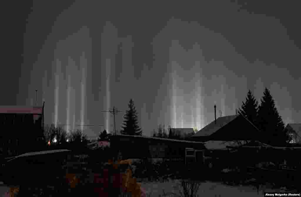 Stâlpi de lumină, un fenomen optic atmosferic, luminează cerul din spatele unor case la Omsk, Russia.