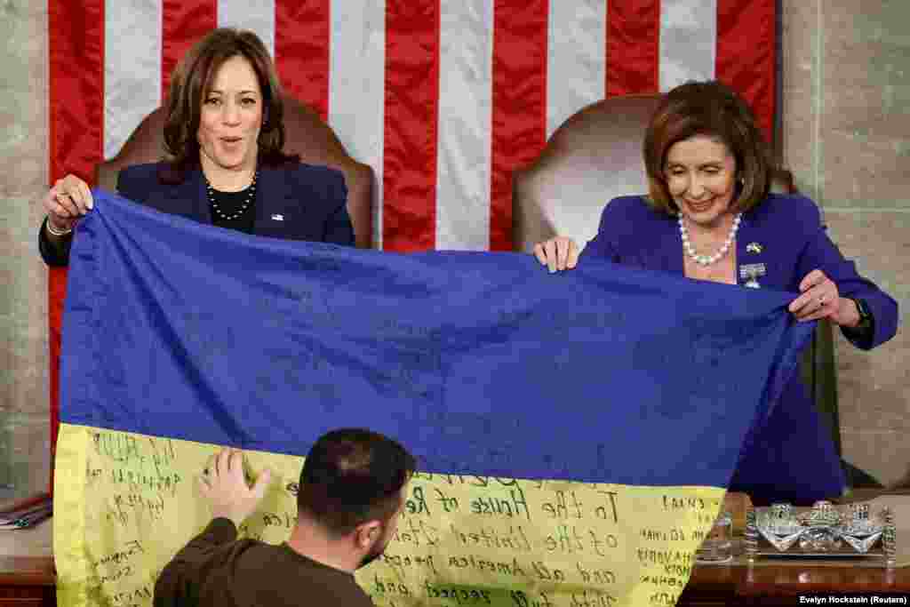 U.S. Vice President Kamala Harris (left) and U.S. House Speaker Nancy Pelosi hold an inscribed Ukrainian flag brought by Zelenskiy from Bakhmut. In his address, Zelenskiy compared the heroism of Ukrainian soldiers defending Bakhmut to that shown by U.S. troops fighting Adolf Hitler&rsquo;s troops in the Battle of the Bulge in 1944, also during the Christmas season. &quot;Bakhmut stands,&quot; Zelenskiy said to cheers. &quot;Ukraine holds its lines and will never surrender.&quot;