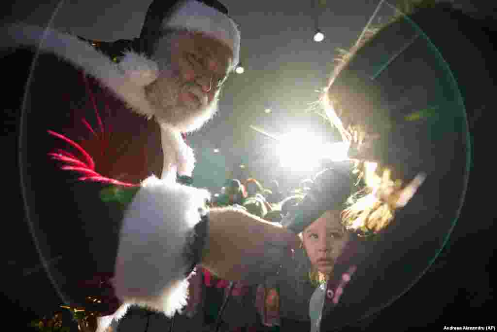 A man wearing a Santa Claus costume speaks to children at an aviation hangar during a Christmas event in Bucharest.