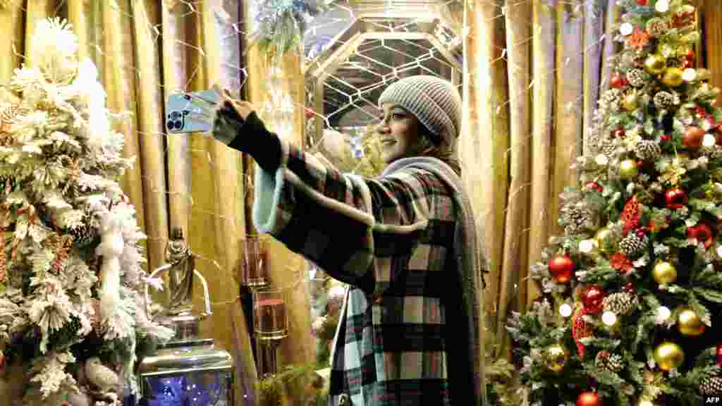 Egy fiatal iráni nő karácsonyfák előtt szelfizik Teheránban december 25-én. Az erkölcsrendészet által a hidzsábtörvény megszegéséért elfogott nőknek kötelező részt venniük egy &bdquo;iszlám értékekről&rdquo; szóló előadáson is