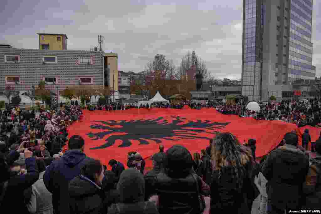 Людзі ў сталіцы Косава, Прышціне, трымаюць гіганцкі албанскі нацыянальны сьцяг падчас святкавання 110-й гадавіны незалежнасьці Альбаніі.