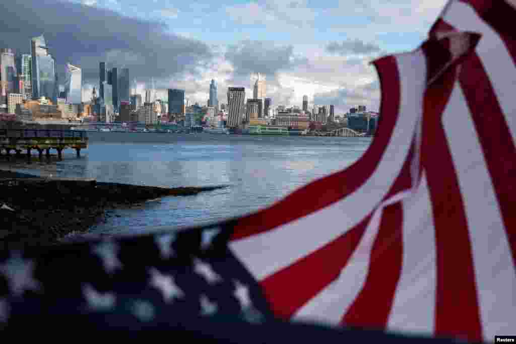 Zastava SAD se vijori dok olujni oblaci prolaze pored Empajer Stejt Bildinga i srednjeg Menhetna u Njujorku, gledano iz Hobokena, Nju Džersi, SAD, 23. decembra 2022