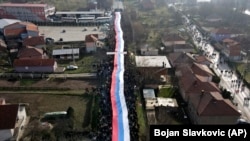 Koszovói szerbek egy óriási szerb zászlót visznek egy tüntetésen a Rudare falu melletti úton lévő barikád közelében 2022. december 22-én