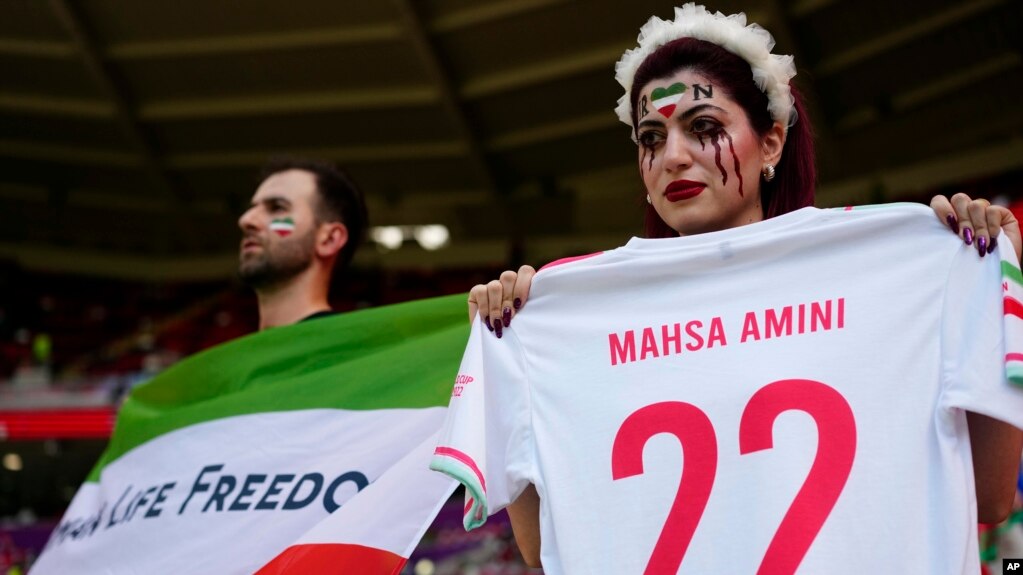 Cổ động viên Iran cầm cờ Iran có dòng chữ "Phụ nữ, cuộc sống, tự do" và chiếc áo sao chép để tưởng nhớ Mahsa Amini bên trong sân vận động ở Qatar trước trận đấu với Xứ Wales ngày 25/11.