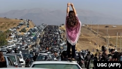 An unveiled woman stands atop a vehicle as thousands make their way toward Aichi cemetery in Saqez, Mahsa Amini's hometown, in the western Iranian province of Kurdistan in late October.