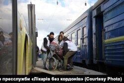 «Лікарі без кордонів» переносять людину в інвалідному візку з автобуса у потяг