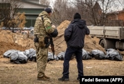 Украинский военный и полицейский возле эксгумированных тел, обнаруженных в массовом захоронении в Буче. 13 апреля 2022 года. Фото: AFP