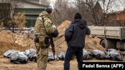 Военнослужащий украинской армии и милиционер стоят возле мешков с трупами, выкопанных из братской могилы, где захоронены мирные жители, в Буче, на окраине Киева, 13 апреля 2022 года, на фоне военного вторжения России в Украину. 