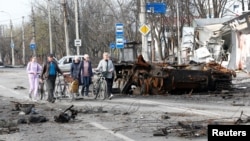 Oameni trecând pe lângă un tanc distrus în timpul conflictului dintre Ucraina și Rusia în orașul-port din sudul Ucrainei, Mariupol, 17 aprilie 2022