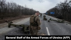Украинские солдаты идут среди уничтоженной российской военной техники после боя в городе Тростянец Сумской области