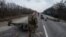 Украинские солдаты идут среди уничтоженной российской военной техники после боя в городе Тростянец Сумской области